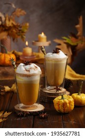 Two glasses with pumpkin spice latte and milk foam surrounded by cinnamon, pumpkins and autumn decoration