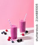 Two glasses of purple wild berry smoothie or milkshake on pink pastel background, copy space for text. Healthy breakfast drink