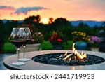 Two glasses of red wine by the flames of a fire table firepit right after sunset.