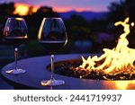 Two glasses of red wine by the flames of a fire table firepit right after sunset.