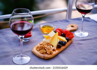 Two Glasses Of Red Wine And Cheese Plate On The Table At The Balcony. Fine Dining At Home.