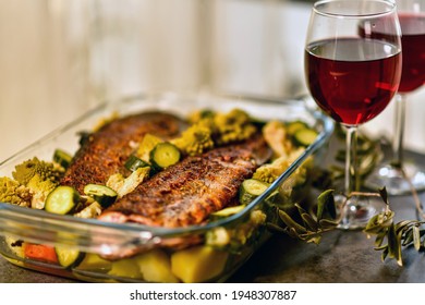 Two Glasses Of Red Wine And A Large Glass Dish With Baked Fish And Vegetables