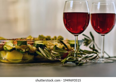 Two Glasses Of Red Wine And A Large Glass Dish With Baked Fish And Vegetables