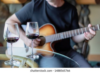 Two Glasses Of Red Wine And Man Playing Acoustic Guitar In The Background