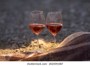 two glasses of red wine are standing on the seashore next to a blanket
