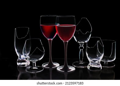 Two Glasses With Red Wine Surrounded By Broken Glasses On A Black Background.