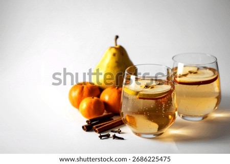 Two glasses of refreshing drinks garnished with apple slices and cinnamon sticks, alongside fresh pears, tangerines, and spices.