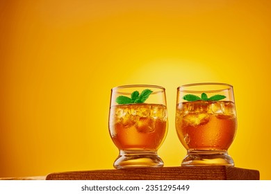 Two glasses of refreshing iced tea with ice cubes and mint leaves on orange background. Studio shot from a low angle with copy space.