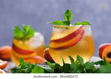 Two glasses refreshing iced tea with peach and mint on a wooden background. Each glass contains slices of fruit and mint leaves. 