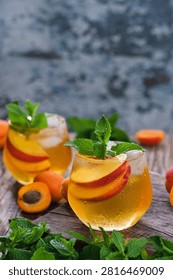 Two glasses refreshing iced tea with peach and mint on a wooden background. Each glass contains slices of fruit and mint leaves.