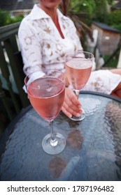 Two Glasses Of Rose Prosecco On A Table. Beautiful Happy Woman Wearing White Dress. Terrace Outside