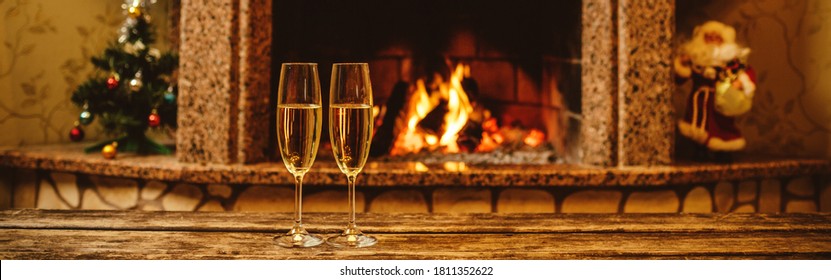 Two Glasses Of Sparkling Champagne In Front Of Warm Fireplace. Cozy Relaxed Magical Atmosphere Staying In A Chalet Home By The Fireside. Snug Holiday Concept. Beautiful Background With Shimmering Wine