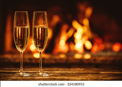 Two Glasses Of Sparkling Champagne In Front Of Warm Fireplace. Cozy Relaxed Magical Atmosphere In A Chalet House By The Fireside. Snug Holiday Concept. Beautiful Background With Shimmering Wine.