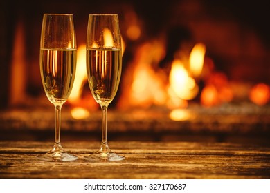 Two Glasses Of Sparkling Champagne In Front Of Warm Fireplace. Cozy Relaxed Magical Atmosphere In A Chalet House By The Fireside. Snug Holiday Concept. Beautiful Background With Shimmering Wine.