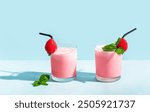 Two glasses of strawberry smoothie or milkshake on blue background, copy space. Healthy breakfast protein rich drink with yogurt and strawberries.