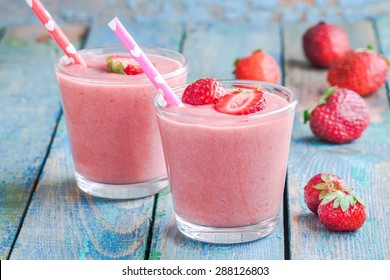 Two glasses of strawberry smoothie with straws on a wooden table