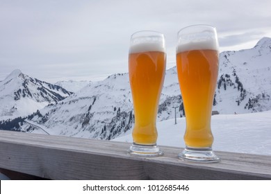 Two glasses of weizen beer at a ski area on a wooden fence