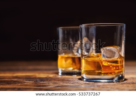 Two glasses of whiskey with ice cubes served on wooden planks. Vintage countertop with highlight and a glass of hard liquor