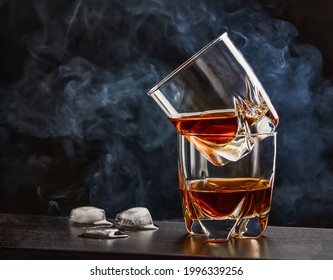 Two Glasses Of Whiskey On A Dark Bar Table, Melting Ice Cubes From The Left Side, Cigarette Smoke At The Background. Close Up, Copy Space