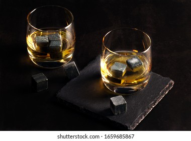 Two glasses of whiskey with stones stand on a dark table. Stones for whiskey on a dark table.