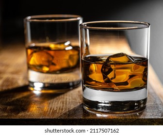 Two glasses of whisky on the rocks on a rustic wooden bartop