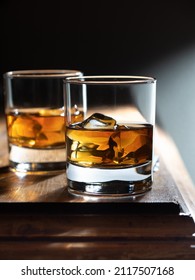 Two glasses of whisky on the rocks on a rustic wooden bartop