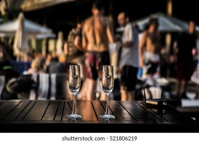 Two Glasses Of White Or Red Vine Against Group Of People. Hot Beach Party. Sexy People. Focus On Empty Glass