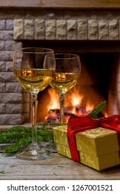 Two glasses of white wine, christmas gift in a box near cozy firepace.