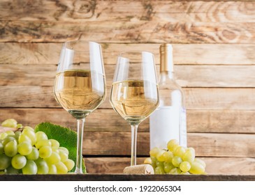 Two glasses of white wine and grape on vintage wooden table. Selective focus