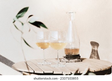 Two glasses of white wine next to an open bottle on a wooden table with an olive branch in the frame on a sunny summer day - Powered by Shutterstock