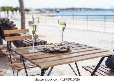 Two Glasses Of White Wine, A Plate With Oysters. Beach, Sea, Trees On The Background 