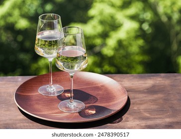 Two glasses of white wine presented on a wooden tray with beautiful sunlight and shadows on dark background. Romantic calm atmosphere. Copy space. - Powered by Shutterstock