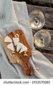 Two glasses of white wine and a wooden plate with cheese and nuts served outside at sunset.