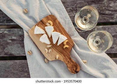 Two glasses of white wine and a wooden plate with cheese and nuts served outside at sunset.