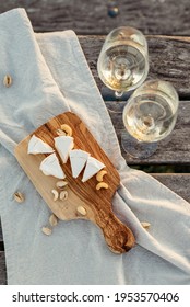 Two Glasses Of White Wine And A Wooden Plate With Cheese And Nuts Served Outside At Sunset.