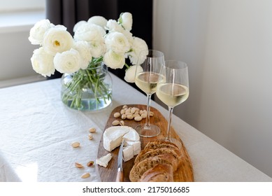 Two glasses of white wine and a wooden board with appetizers on the table.