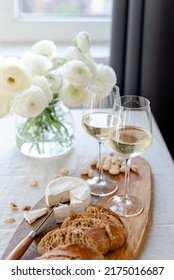 Two glasses of white wine and a wooden board with appetizers on the table. - Shutterstock ID 2175016687