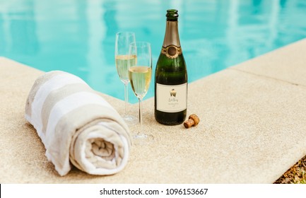 Two Glasses Of Wine With Bottle Of Sparkling Wine And Soft Cotton Towel On Side Of A Swimming Pool Edge.