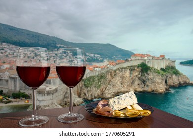 Two glasses of wine with charcuterie assortment against view of Dubrovnik, Croatia. Glass of red wine with different snacks - plate with ham, sliced, blue cheese. Romantic celebration.