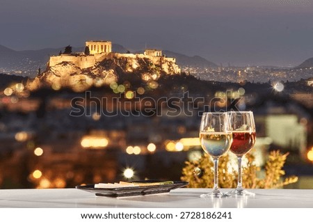Two glasses of wine on a table with a view of the Acropolis at night.