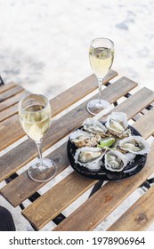 Two glasses of wine wine and a plate with oysters and limes on a wooden table. Outdoors, sunny weather 