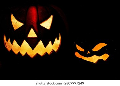 Two glowing, menacing jack-o'-lanterns featuring scary carved faces are dramatically illuminated in the darkness.