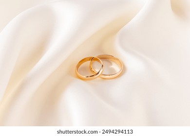 Two gold classic wedding rings lie on a chic satin fabric with soft pleats. wedding background. Layout for the designer and product advertising