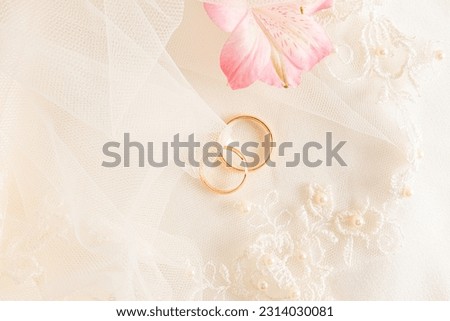 Two gold engagement rings and pink astromeria flower on a beige satin background. Wedding background. A copy space