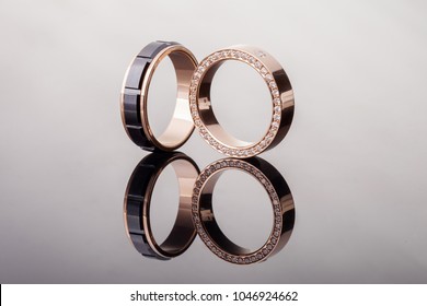 Two Gold Wedding Rings With Diamonds And Black Ceramic Close - Up With Reflection