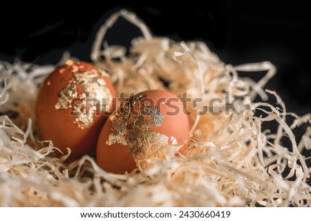 two gold-covered eggs decorated for Easter in a straw nest