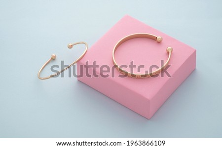 Two golden bracelets on pink box on blue background with copy space