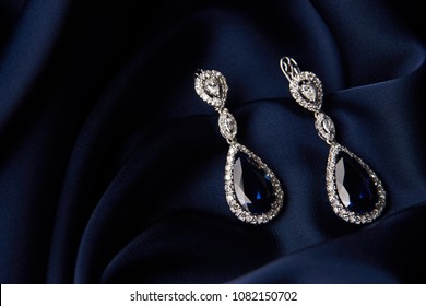 Two Golden sapphire earrings with small diamonds. Pair of platinum earring with sapphire gemstone on blue satin background. Luxury female jewelry, close-up