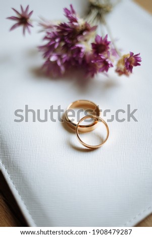 Two golden wedding rings and pink flowers on white background. Vertically framed shot.