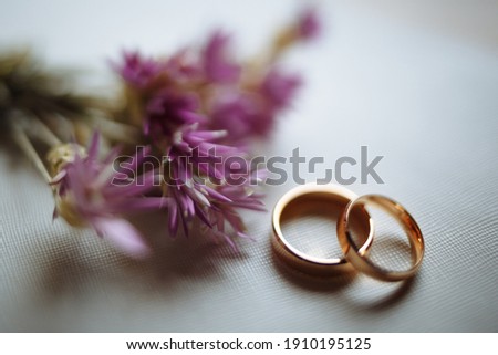 Two golden wedding rings and pink flowers on white background. Horizontally framed shot.